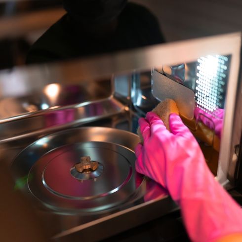 Wipe Out The Crumbs A person wearing pink rubber gloves, cleaning microwave.