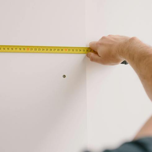 1. Size Matters Person holding up a yellow measuring tape to a white wall measuring to make sure there is enough space before storing holiday decorations for Home Network