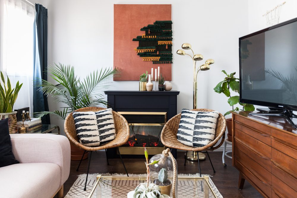 Fine Balance two wicker chairs with black and white cushions in front of black fireplace and brass floor lamp