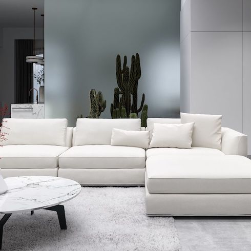 Wide Open Spaces Cloud couch dupes featuring Rove Concepts Milo Modular Sectional in a low lit modern living area with a grey shag on a grey wood floor, a round marble topped coffee table and a large potted cactus in the background