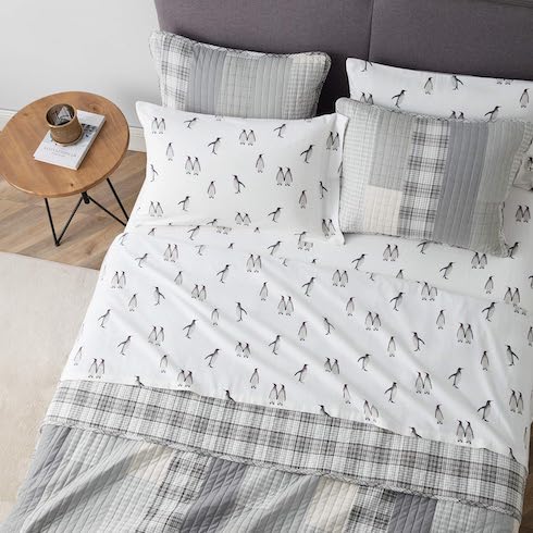 Fluffy Flock Eddie Bauer Rookeries Flannel Sheet set from Amazon.ca on a dark grey upholstered bed with a patchwork quilt comforter and four pillows, in a bedroom with wood floors, a cream coloured rug, and a wooden bedside table with hairpin legs and book and mug on top