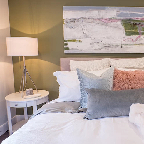 Sage Advice Beautiful bedroom with a sage green feature wall and large piece of art, a pink bed with white and grey bedding and a small round bedside table with a white lamp as featured on Home Network.