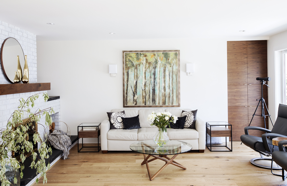 Colour Coordinated light sofa with black and white cushions, painting of trees and round glass top coffee table