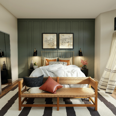 At Ease A gold framed bed against a dramatic steel blue accent wall in a chic bedroom with a wood and cane bench seat, black and white striped rug, two black and gold wall scones, two black bedside drum tables, two black framed drawings above the bed, black and white curtains, and a large wall mirror