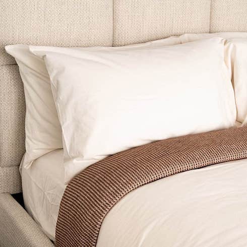 History Lesson Skylark & Owl’s Organic Flannel Sheet Set in Chalk and Organic Flannel Duvet Cover in Chalk are featured on an upholstered bed with a stack of pillows and a brown blanket