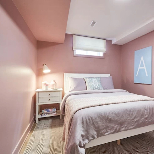Barbiecore Basement bedroom from Extreme Makeover: Home Edition on Home Network is painted in all over petal pink with a double bed with pink and white bedding and a side table and area rug