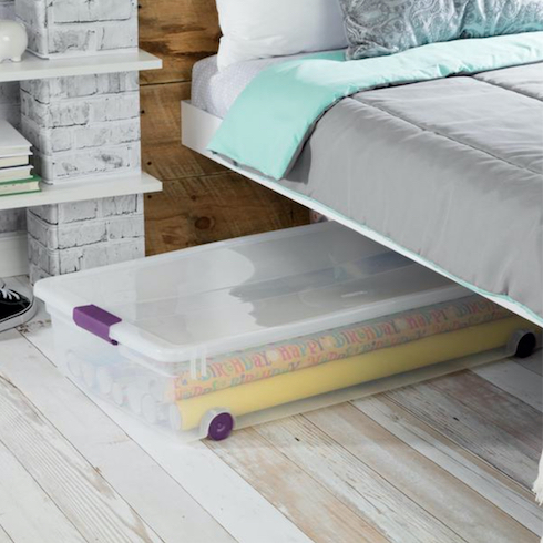 3. Flat Out Sterilite ClearView Wheeled Underbed Storage Box half tucked under a bed on grey wood floors as part of Home Network The Secret to Storing Holiday Decorations in Small Spaces