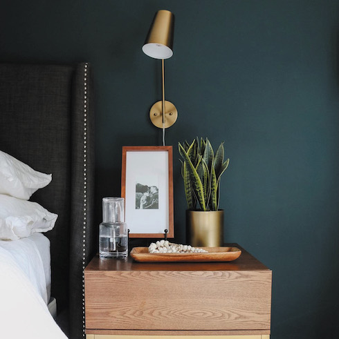 Deep Waters Sherwin-Williams Cascades SW 7623, a dark, majestic blue paint colour, exudes a rich and mysterious personality with its swirl of grey, yellow and blue undertones featured on the walls of the chic small bedroom with a side table and upholstered headboard