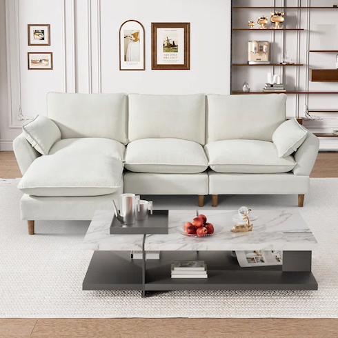 Small-Space Saver Cloud couch dupes featuring a Tetiana L-shape Upholstered Cloud Modular Sofa in Beige Chenille from Wayfair in a white living room with a large white area rug, a modern marble and black coffee table, and white wall with moulding and hung art