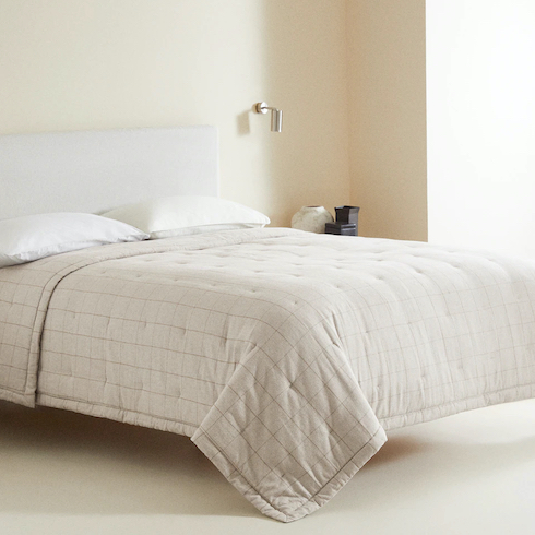 Windowpanes to Our Soul Zara Home Flannel Quilt with contrast check print on a white upholstered king sized bed in a chic cream coloured bedroom with cream coloured carpet, a silver lamp, large white urn and two black boxes in one corner