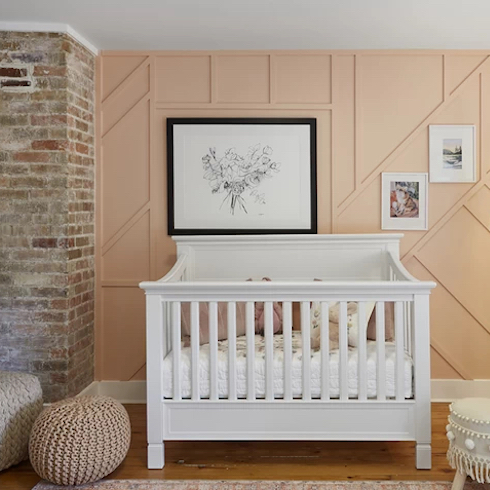 Just Peachy Beautiful nursery with a white crib, two woven floor poufs, an exposed brick chimney and a panelled wall painted a pretty peach colour.