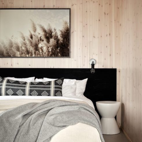 Black and White Thinking Guest bedroom at Wander the Resort featuring an extra wide black headboard, large grass artwork, light wood wall panelling, bed with white sheets and black pillows, and a drum bedside table