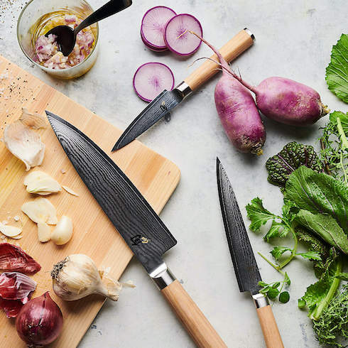 A Sharp Mind Set of Shun blonde handled knives on a grey countertop with a chopping board, garlic, onions, radishes, and green parsley as part of HGTV's 10 Gift Ideas for the Women in Your Life