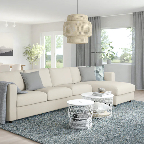 Finally, Finnala Cloud couch dupes featuring Ikea FINNALA sofa with a chaise lounge in Gunnared beige in a large living and dining area with light wood floors, large grass pendant lamp, a grey area rug, two white metal basket coffee tables, white walls, and grey gauzy drapes