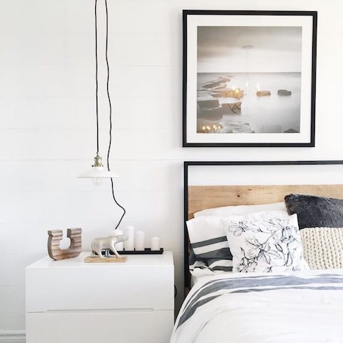 Model Life Chic black and white bedroom designed by Ottawa-based Leclair Décor featuring a black framed bed, black framed wall art, a white bedside table with a polar bear statue, a tray of white candles and a white pendant lamp with a black cord.