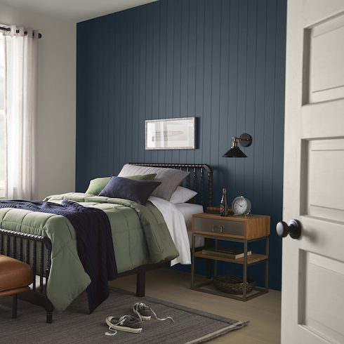 Midnight Rain Cool small bedroom featuring Behr paint colour Midnight, a black framed bed with green and blue bedding, and a grey floor with an area rug with a pair of shoes on it.