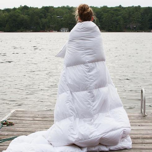 Au Lit Fine Linens Woman with duvet cover overlooking lake.