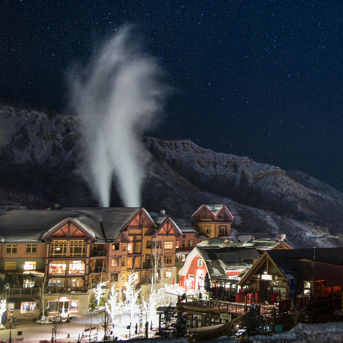 Aspen Snowmass, Colorado Aspen Snowmass Ski Resort at night with lit up buildings and snow making machines at work.