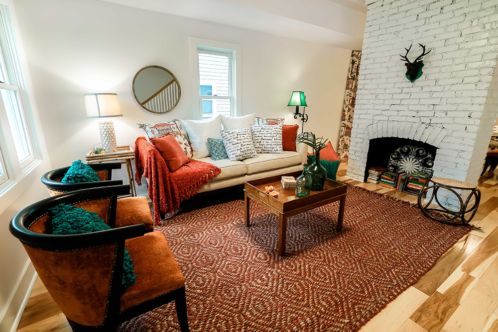 Show Off Your Literary Collection Modern living room with geometric rug and warm-toned furniture. Inside a whitewashed brick fireplace is a stack of books.