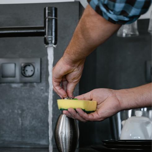 9. Sanitize Your Sponges a person washing a yellow cleaning sponge