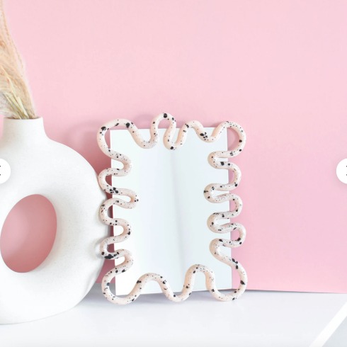 Painted Mirror A squiggle-shaped mirror on a white ledge in a pink room.