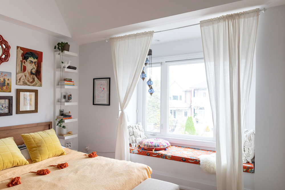 Window Seat Yellow bed with gallery wall above and white floating shelves beside and window seat
