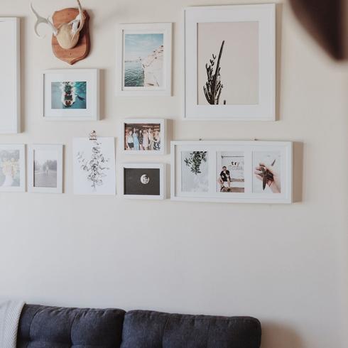 Hang a Gallery Wall A gallery wall with white photos in white frames mounted on the wall.