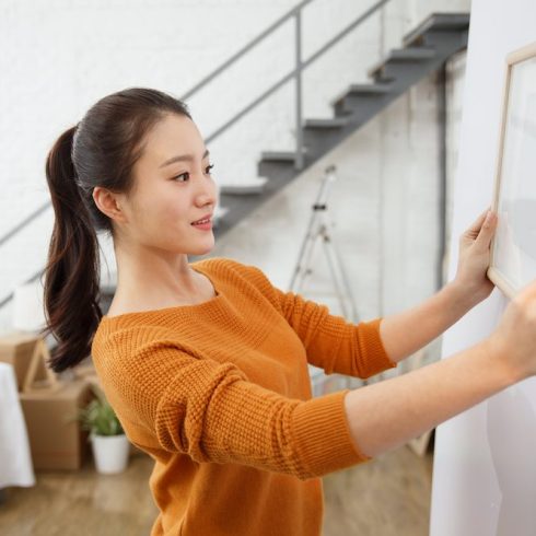 Step Seven: Hang Your Picture woman hanging framed photo on white wall