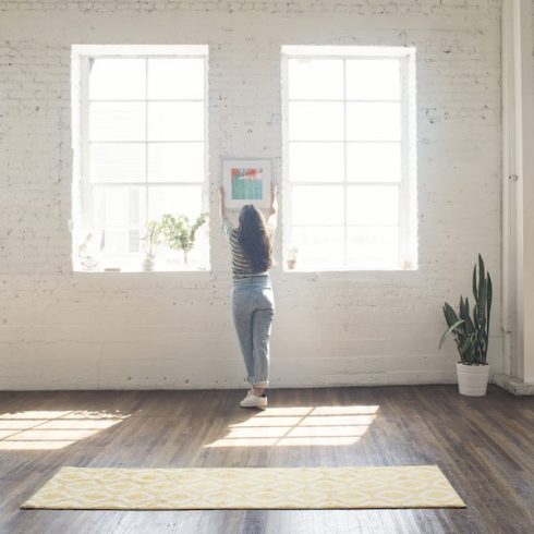 The No-Nail Method woman attaching picture frame to white brick wall in a loft
