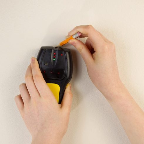 Find the Studs hands using stud finder on beige wall
