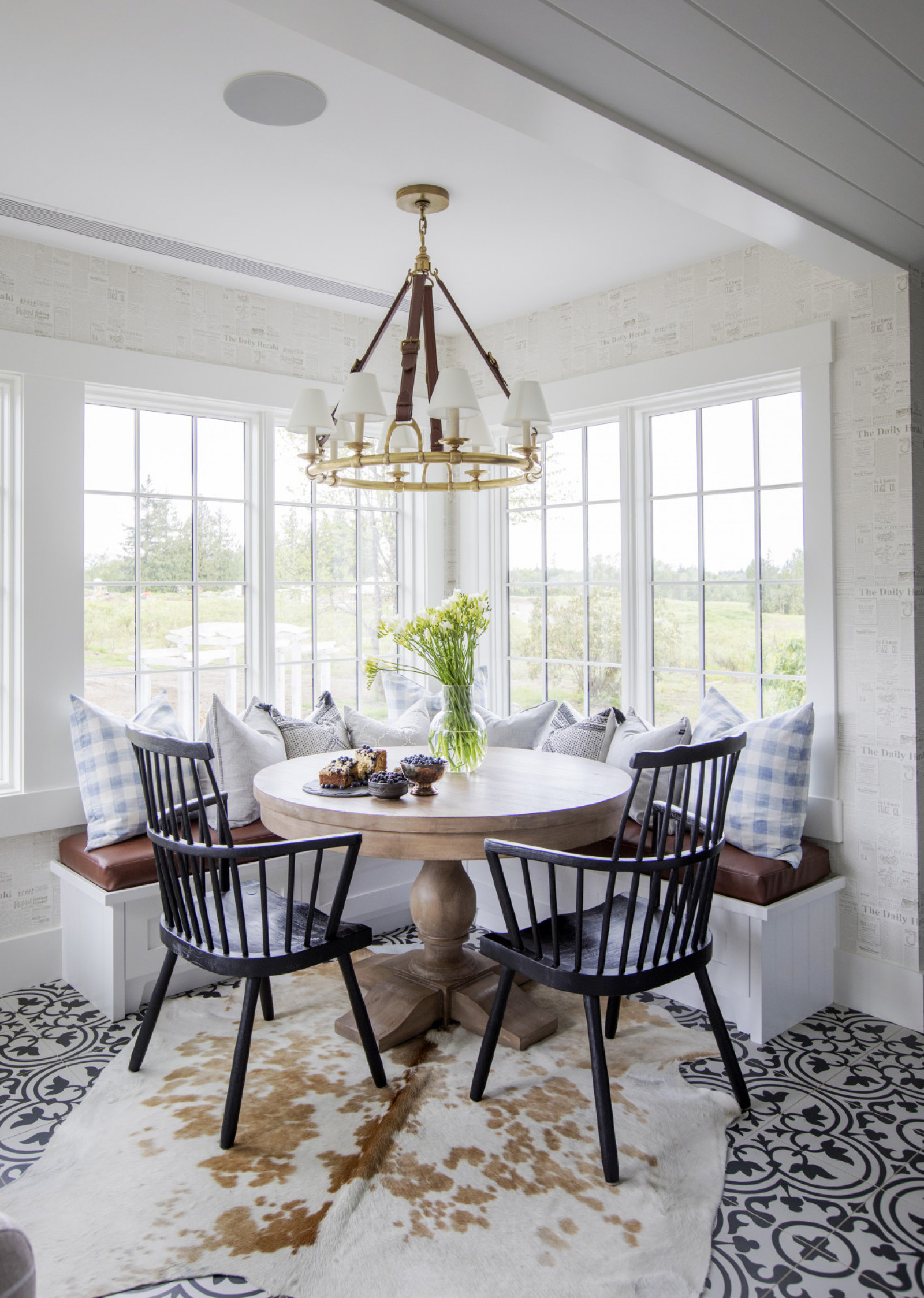 Corner Lot corner of windowed eating nook with built in seating, round table and two black chairs on hide rug, black and white tiled floor