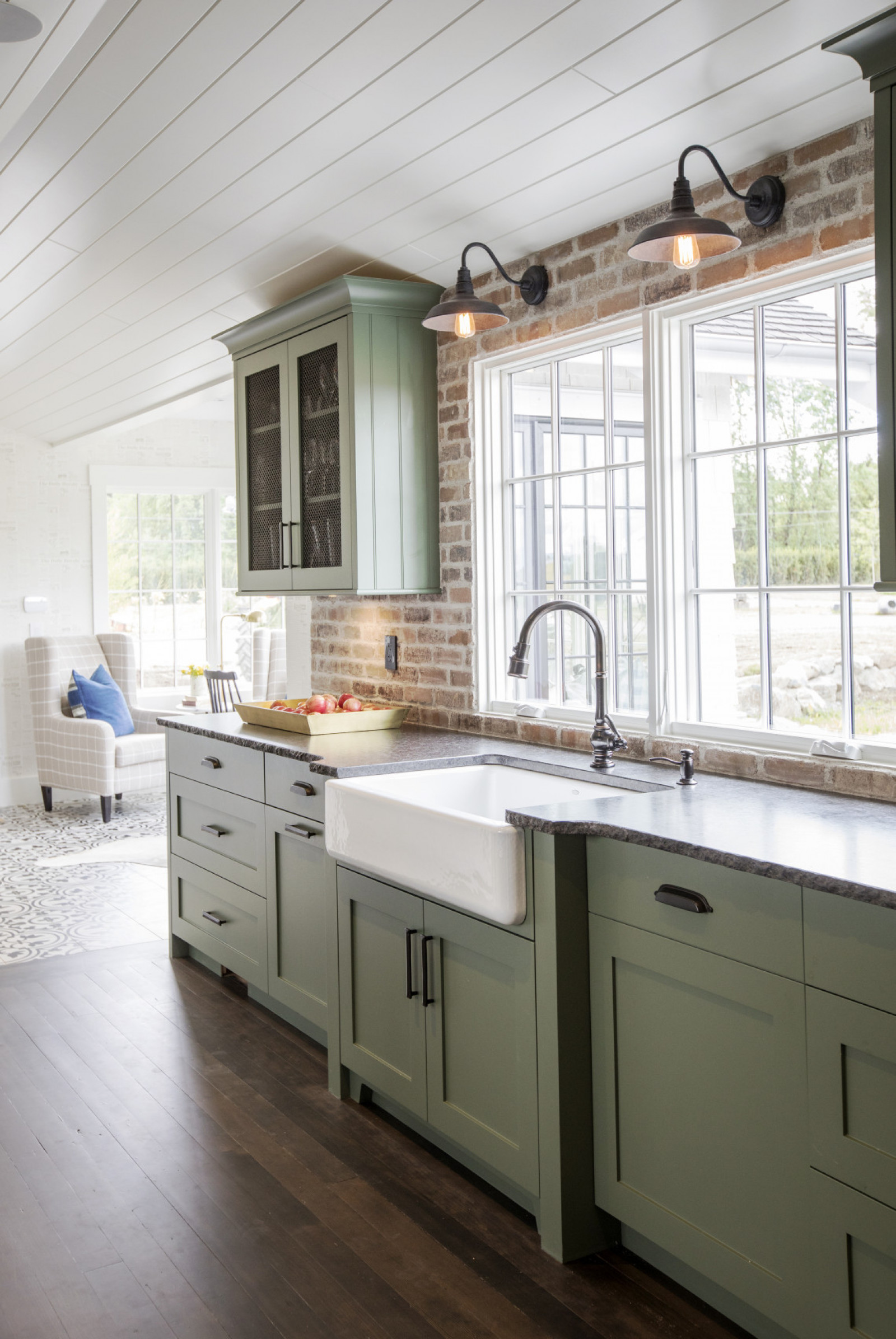 Farm Fresh white apron sink in front of kitchen window with green cabinets and two sconces above