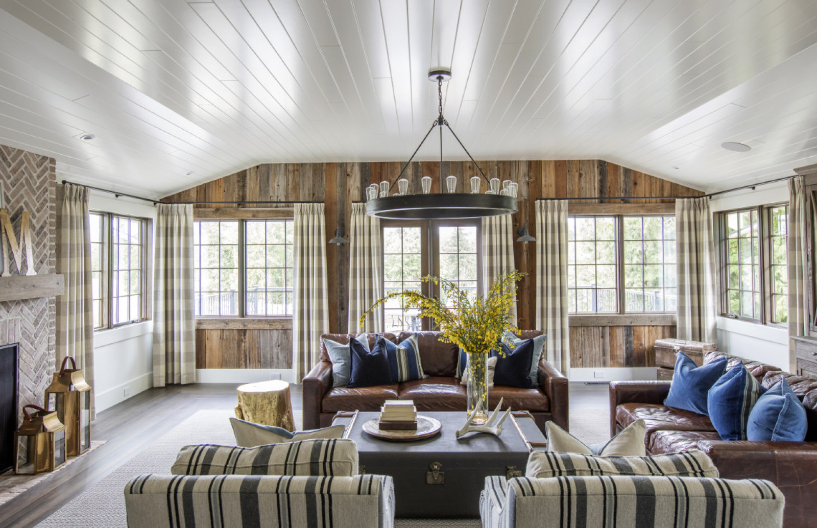 History Lesson living room with white wood ceiling, wood plank walls, windows, two brown leather sofas, two striped arm chairs