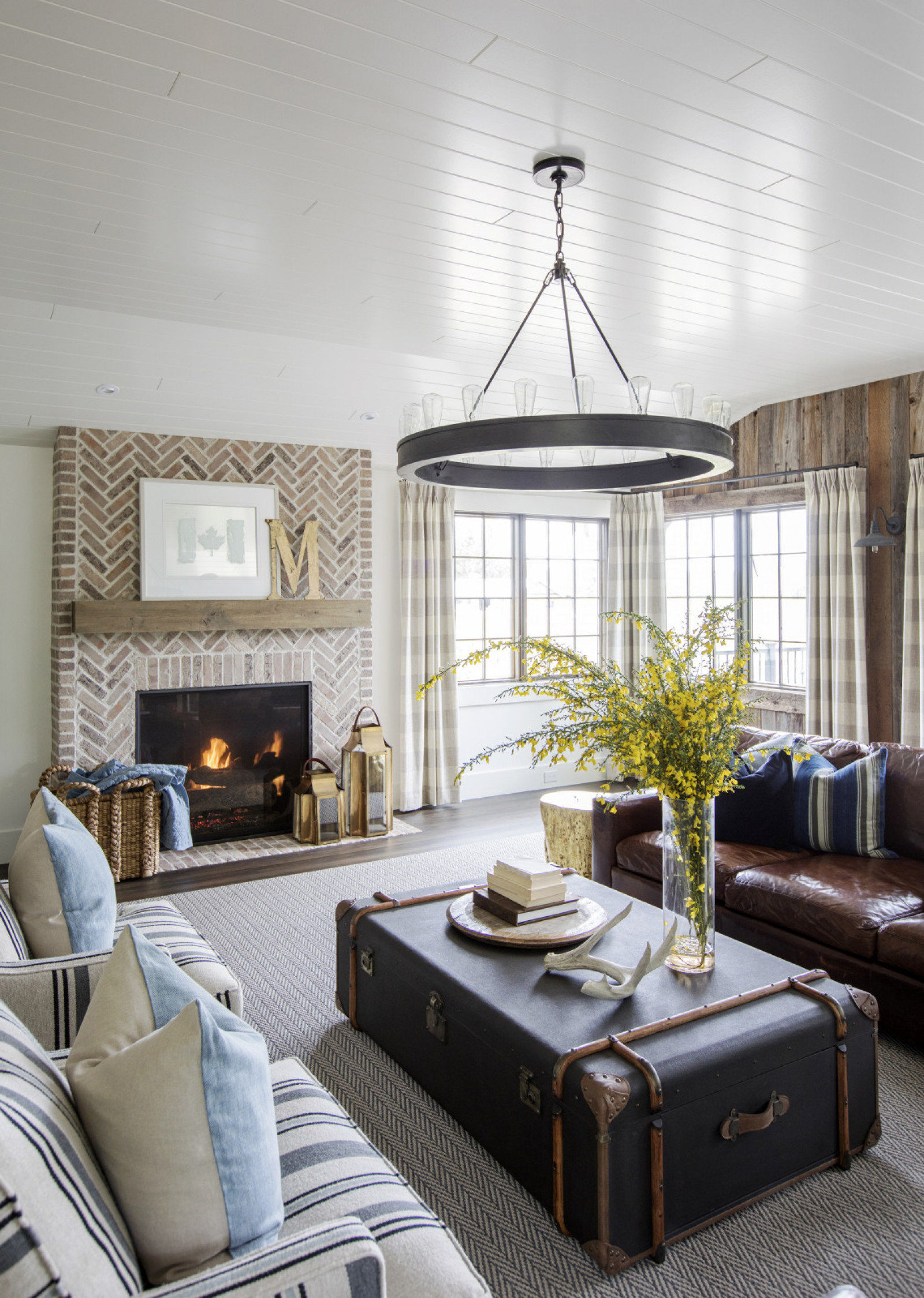 Old Meets New farmhouse living room with brick fireplace, chevron rug, trunk as coffee table with forsythia arrangement on top