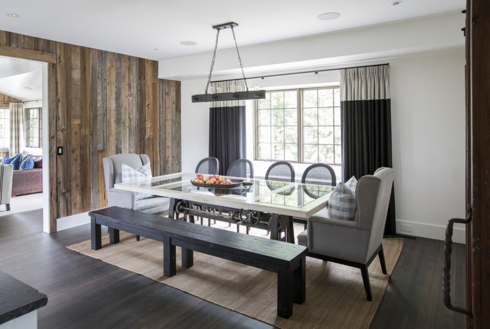 In the Mix farmhouse dining room with black bench, two wing backs, four chairs, glass insert table, black drapes