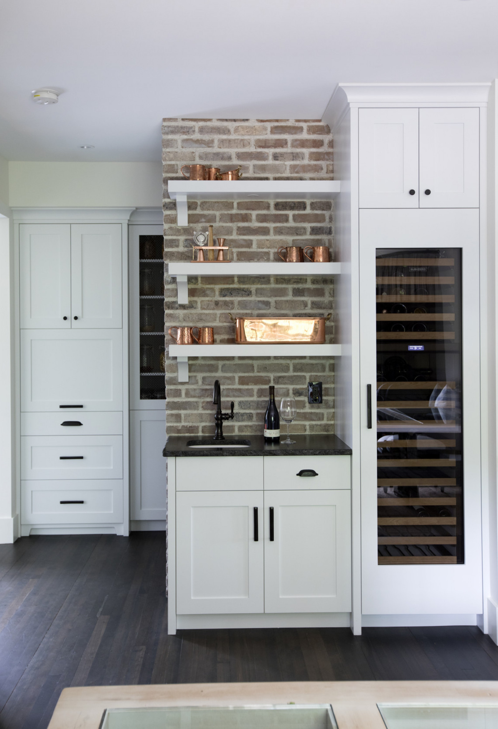 Wine Not? exposed brick wall with floating shelves beside wine fridge in kitchen