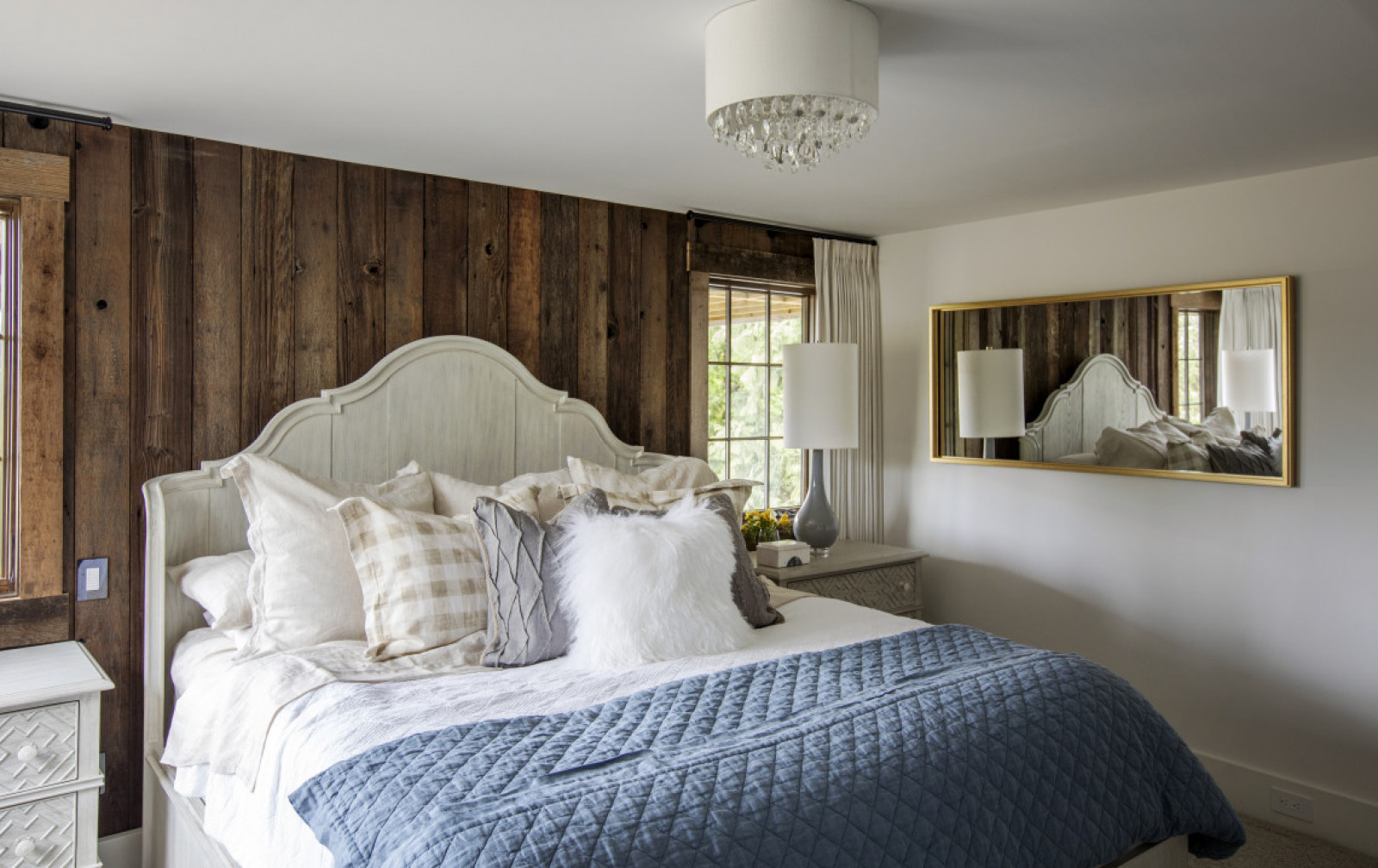 Master Class bedroom with wood plank wall, gold frame mirror on one wall, blue quilt, lots of cushions, white furry one in front