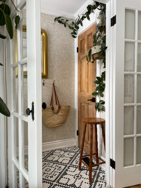 A Warm Welcome An entranceway with door, crawling plant, mosaic tile flooring and a straw bag hanging on the wall