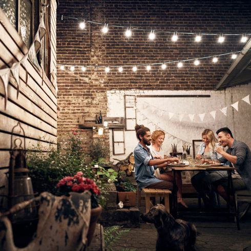 Mistake #6: Not Making the Most of Your Side Yard Small backyard with string lights and friends eating dinner at table.