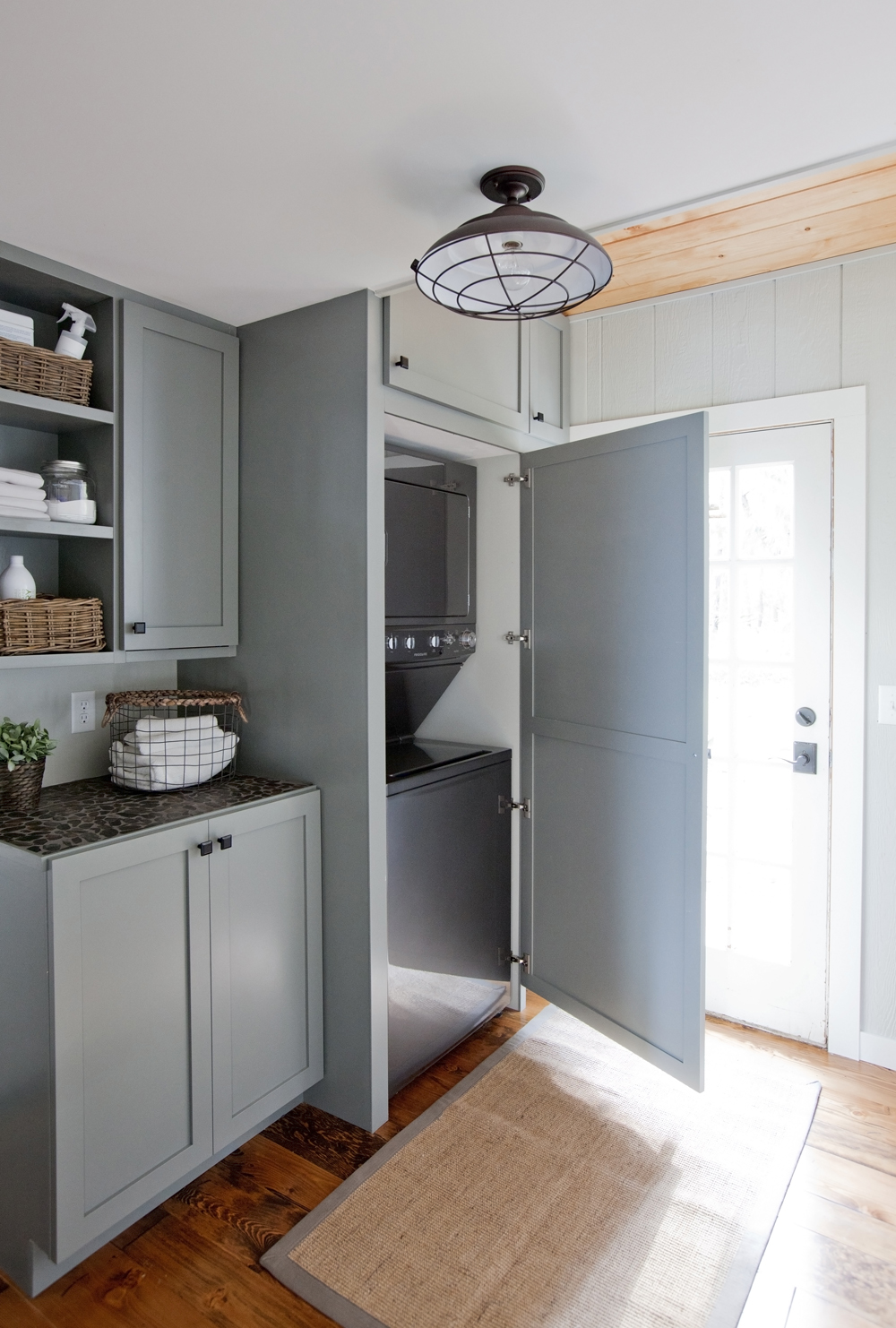 Hide Away Bright laundry room with grey-blue custom cabinetry and washer and dryer concealed behind cupboard.