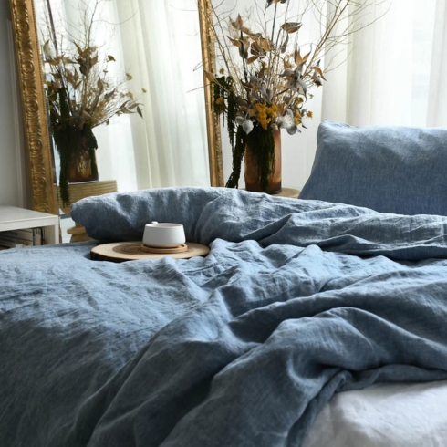 Flax Planet A bed covered in cozy blue linen duvet cover and pillowcase with a cup of coffee on top.
