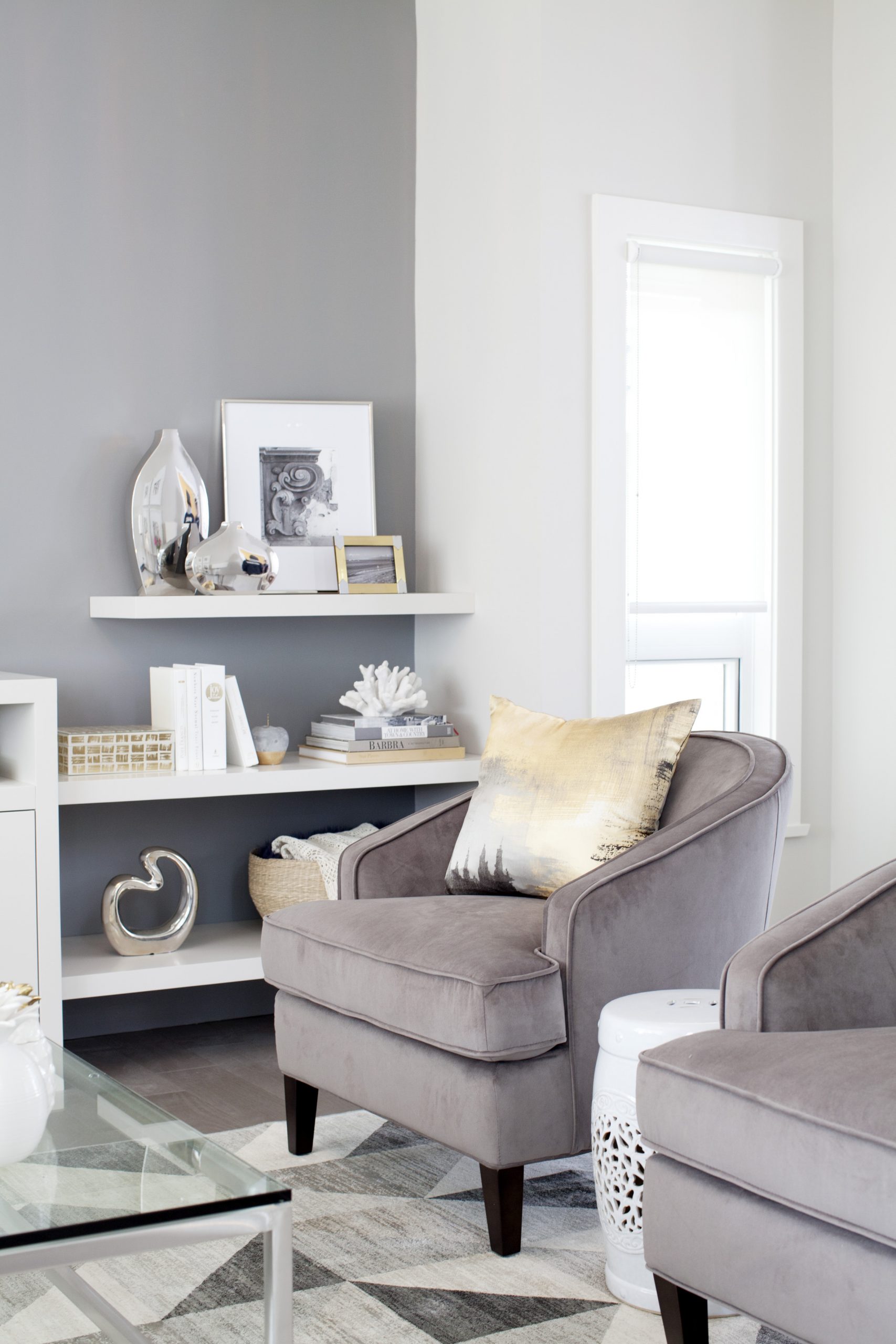 Shades of Grey one grey wall with white shelves and two grey velvet armchairs