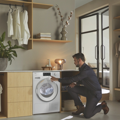 4. Sustainability Rules A male loading his sustainable Miele dryer, a home appliance trend for 2025