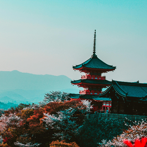 Kyoto, Japan A red and black temple on a hillside with blooming trees in Kyoto, Japan with mountains in the background.