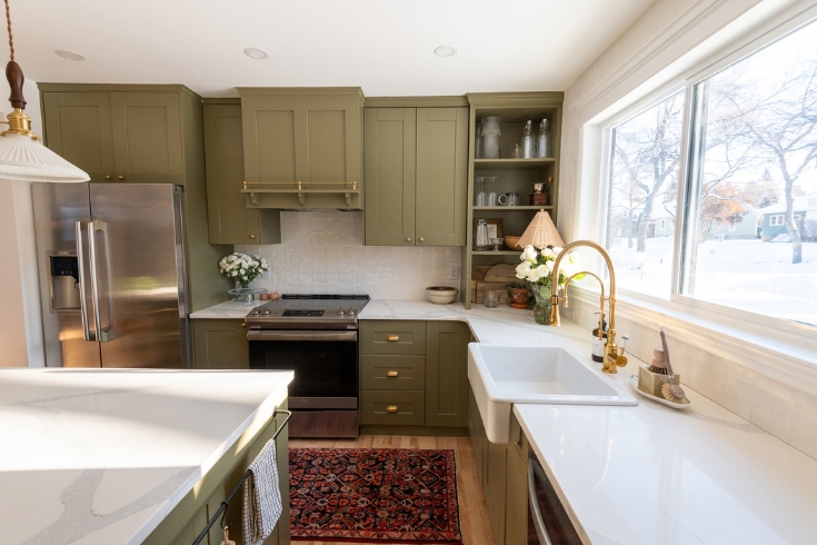 Learning Curve A kitchen with a large window, green cabinetry, gold fixtures and quartz countertops