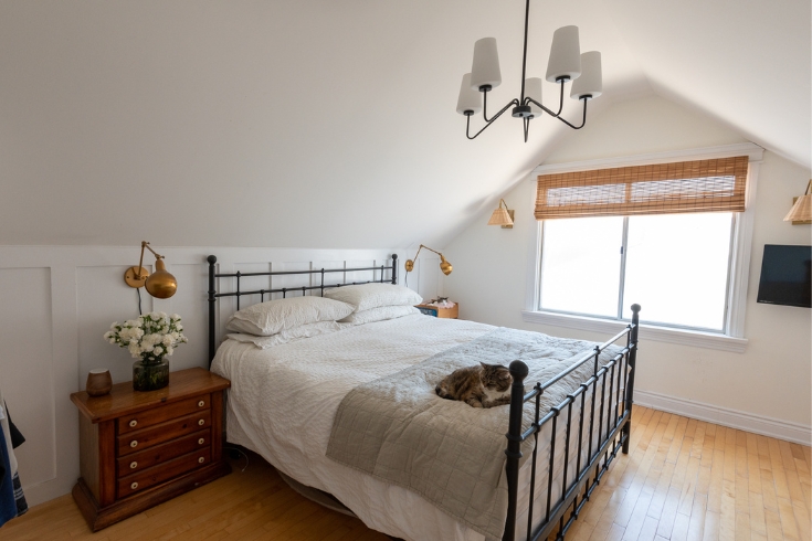 A Work in Progress A large primary bedroom with sloped ceilings, large window, and a cat on the bed