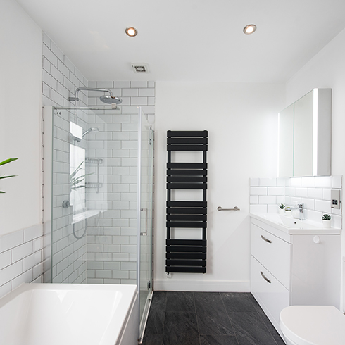 Grout A general interior view of a white half rectangular tiled and painted bathroom, bathtub, glass shower cubicle, chrome taps and shower head, window and potted dragon tree plant, sink mounted to a vanity unit, mirror medicine cabinet and black towel warmer radiator and a picture frame with the words saying