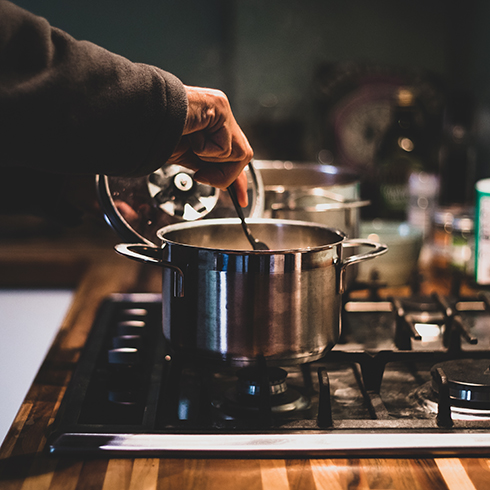 Stainless steel surfaces A man cooking at night, stirring the stew pan. People who eat home-cooked meals on a regular basis tend to be happier and healthier.