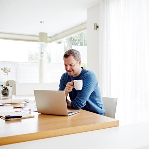 Choose the Right Desk TitleMan working at home using laptop drinking coffee