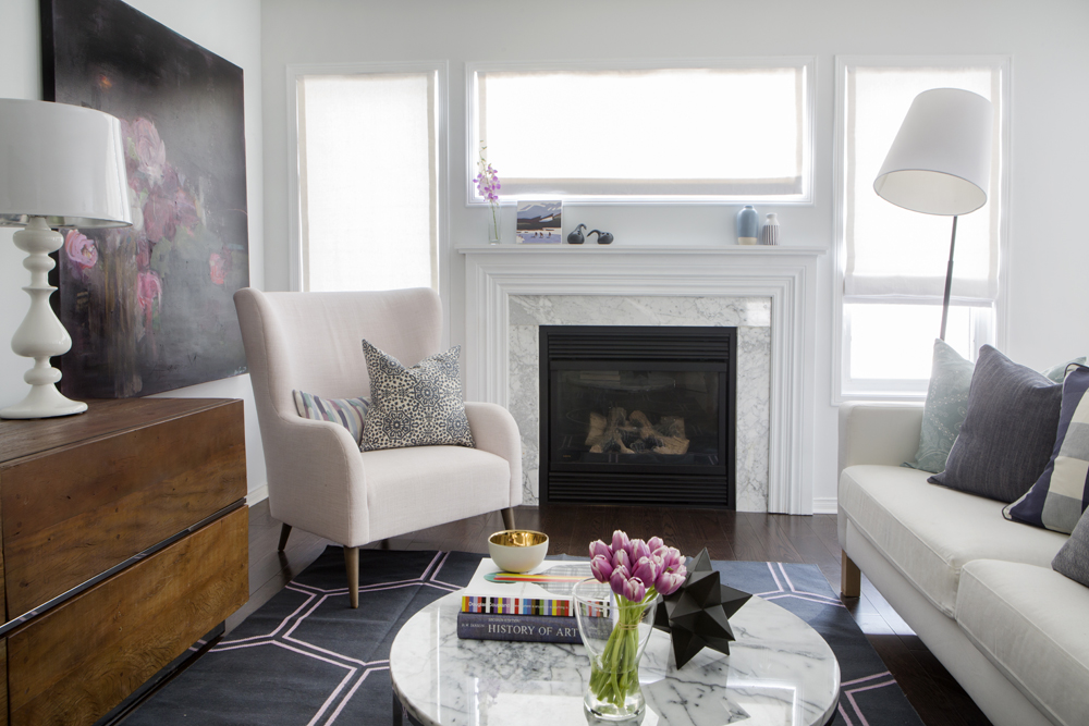 Big Time white and marble fireplace framed by windows with over-sized armchair in front of it